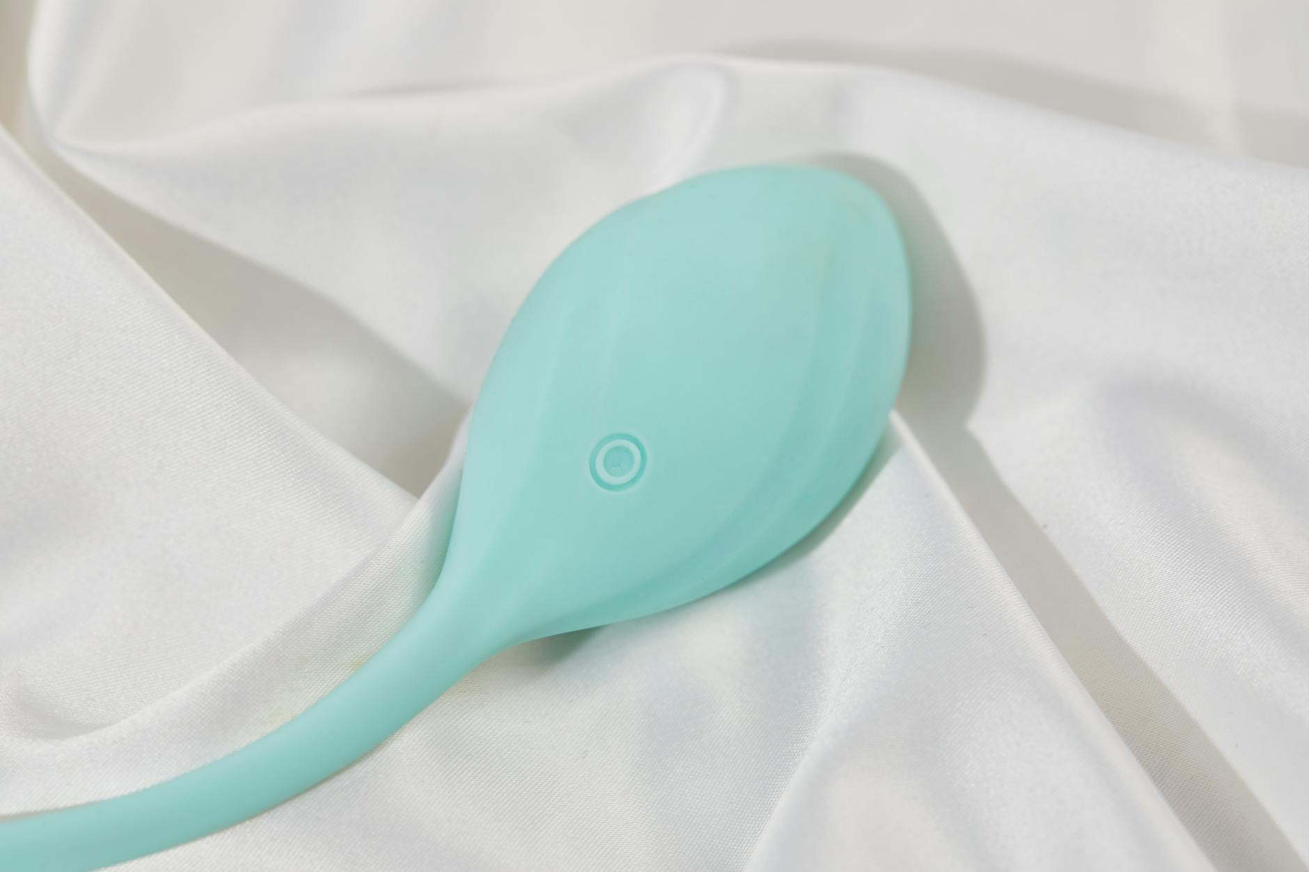 A sleek teal clitoral vibrator resting on white silk fabric