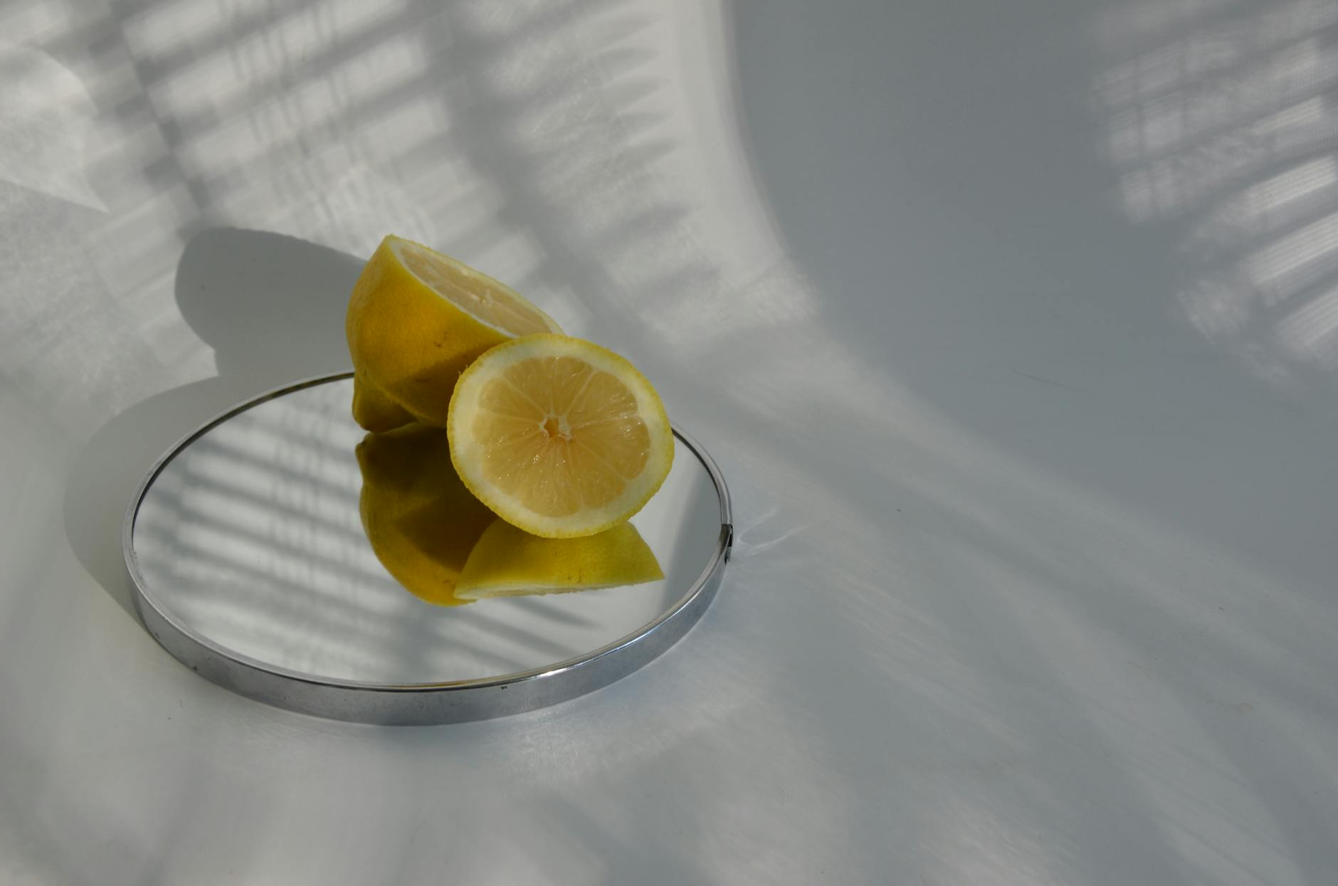 Sliced lemons on a mirror casting shadows in minimalistic food photography.