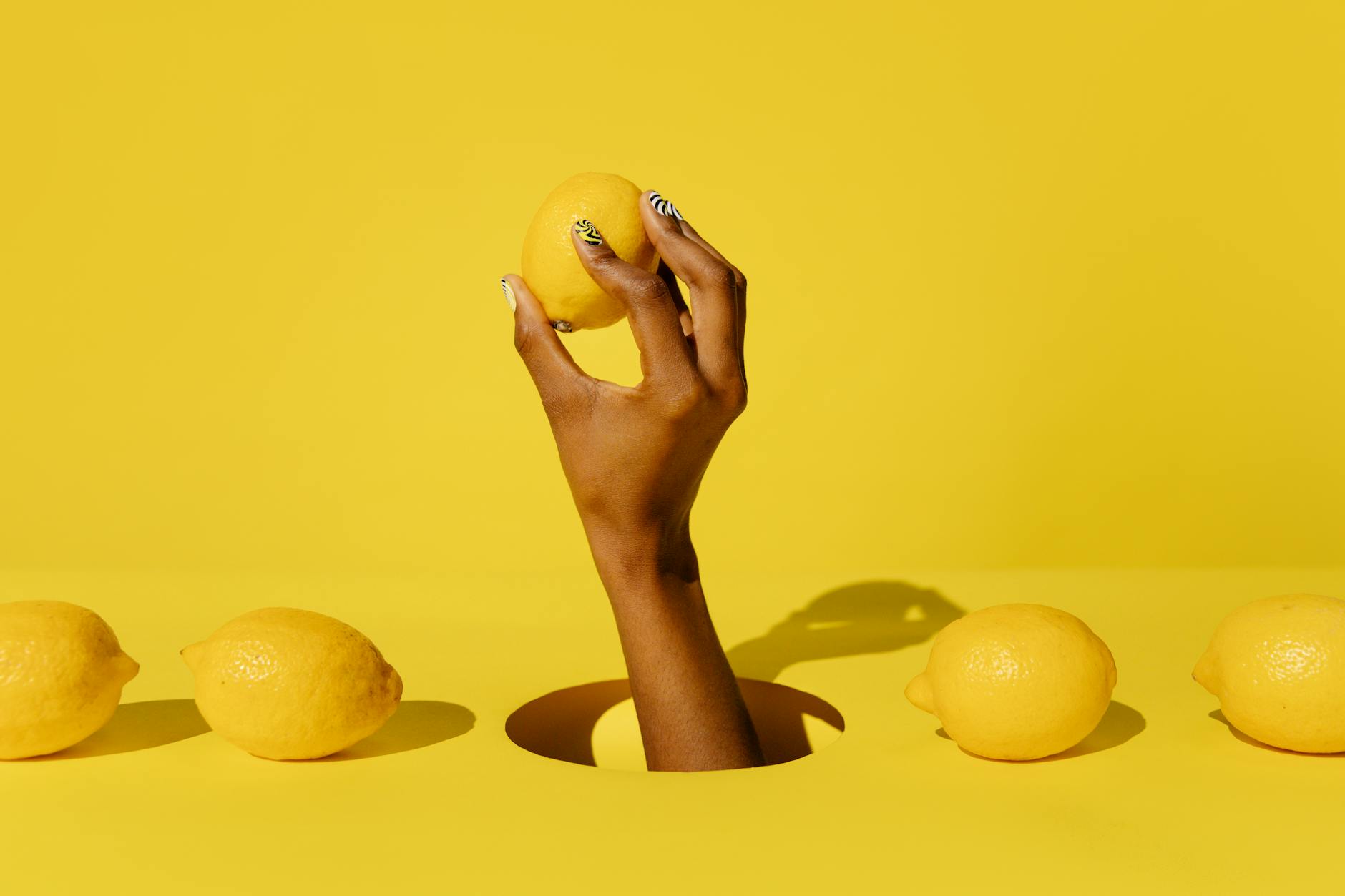 Hand holding a fresh lemon against a vibrant yellow background