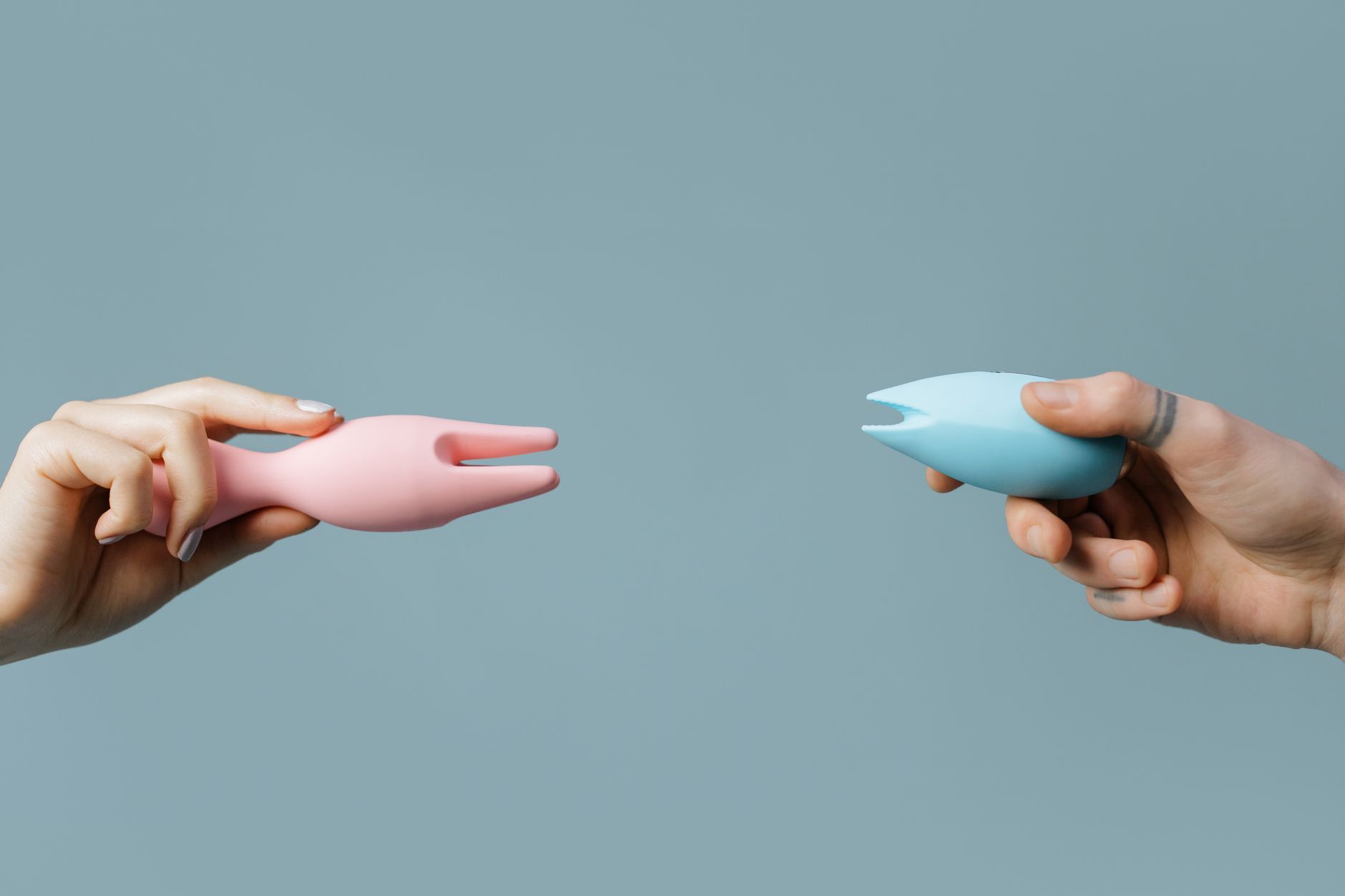 Two hands holding lemon vibrators against a pastel background during intimate exploration