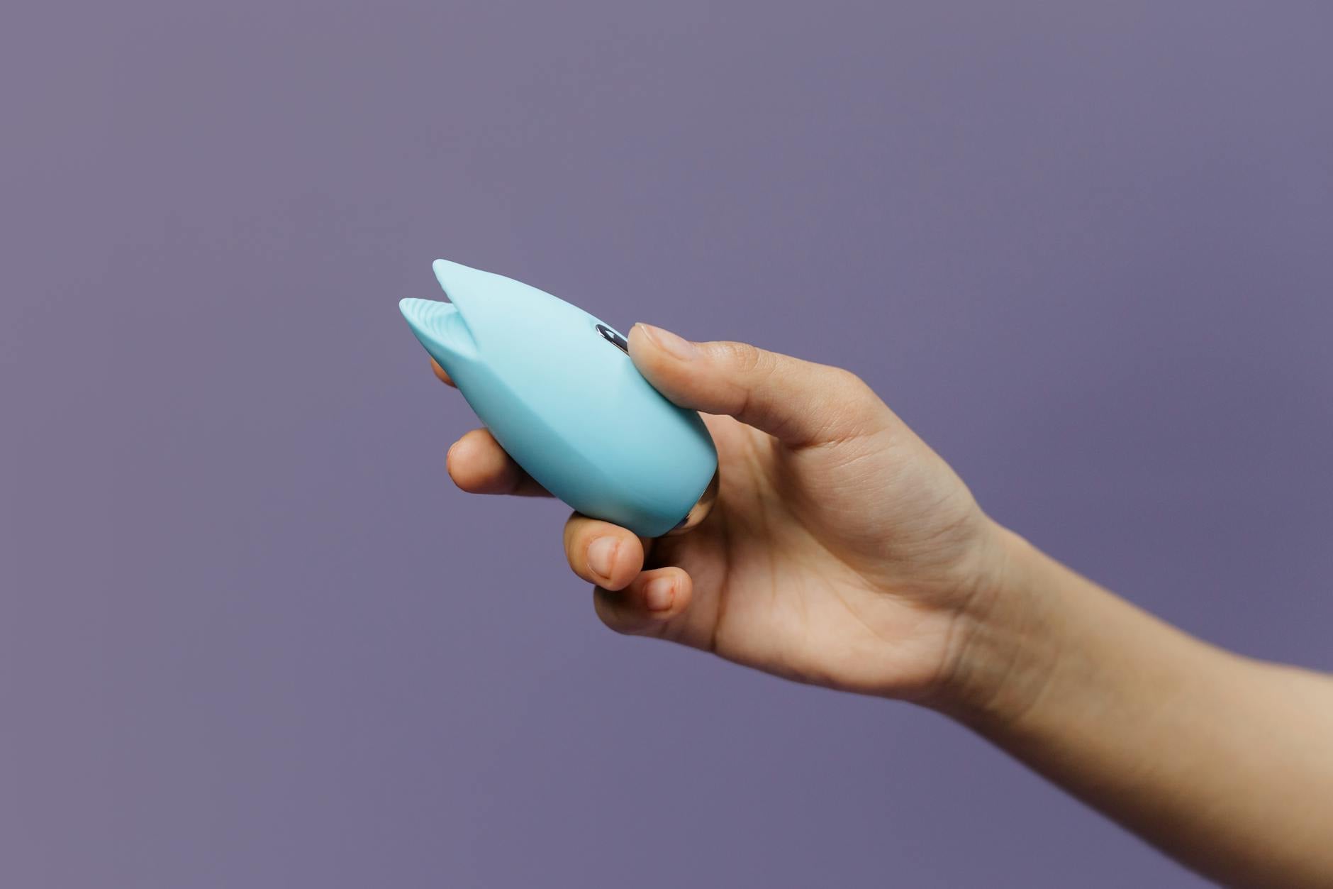 A blue silicone clitoral vibrator in hand against a purple background, symbolizing self-pleasure and confidence