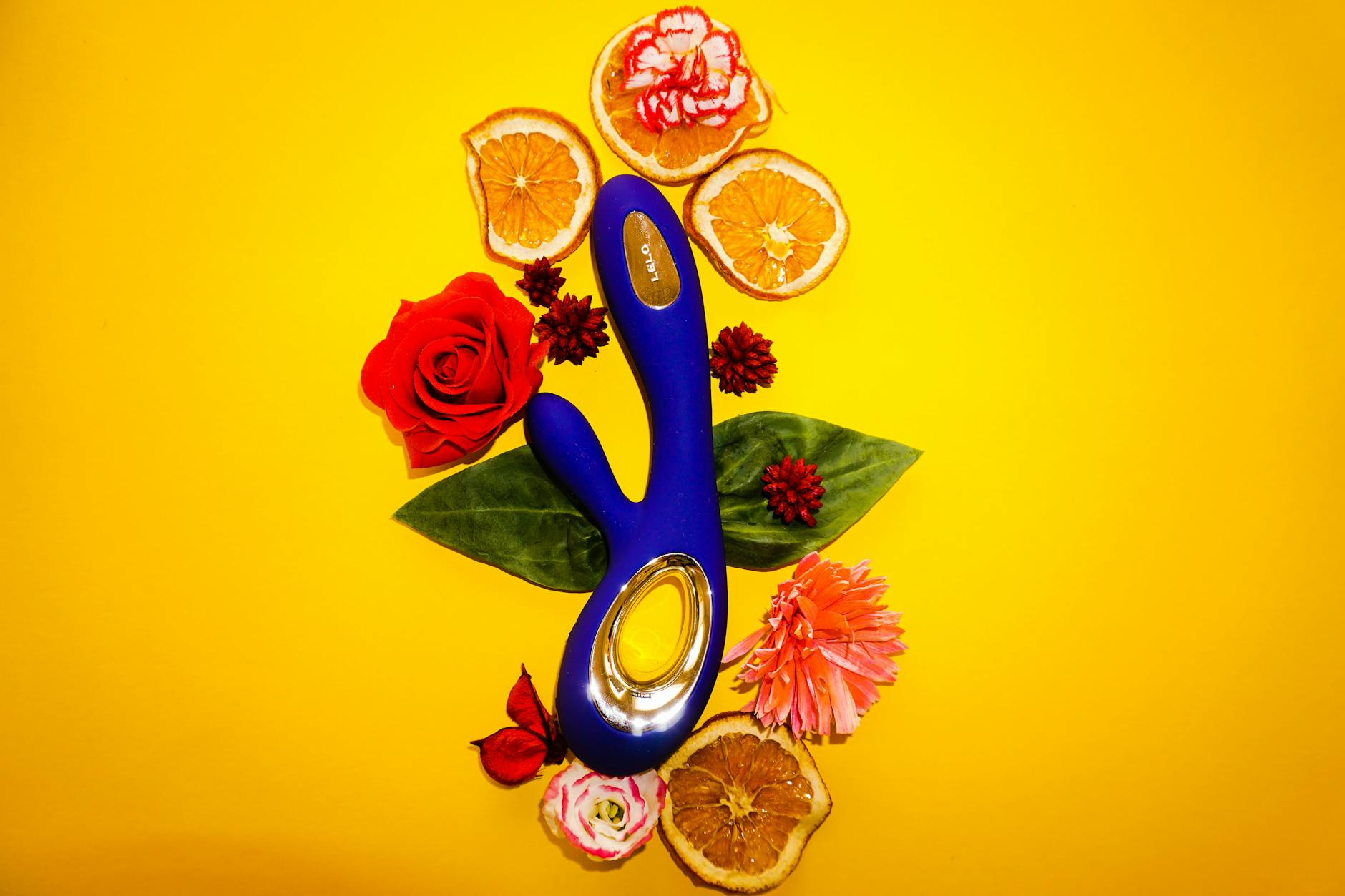 A lemon-yellow vibrator surrounded by fresh lemons and citrus slices on a bright yellow background