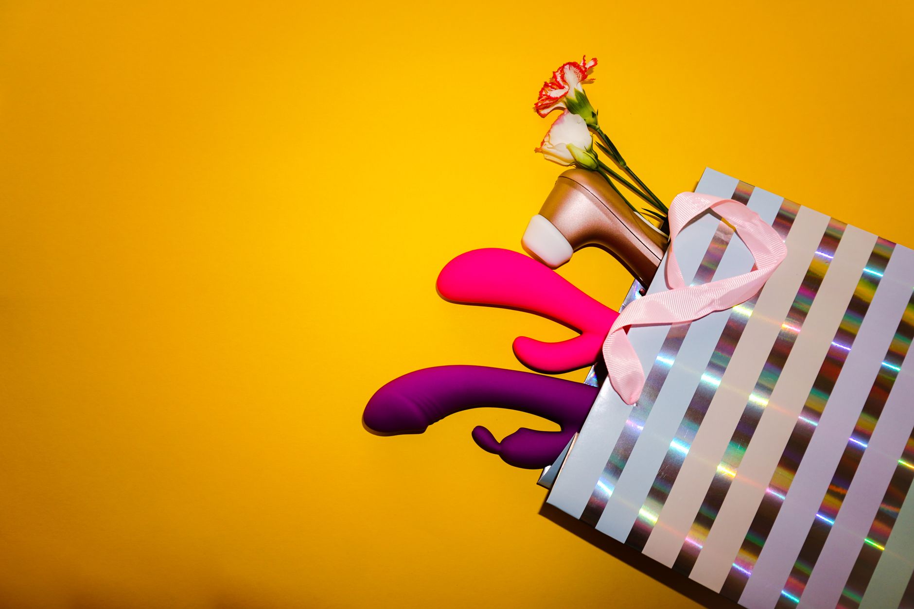 Studio display of colorful sex toys on bright yellow background, showing varied vibrator designs and shapes