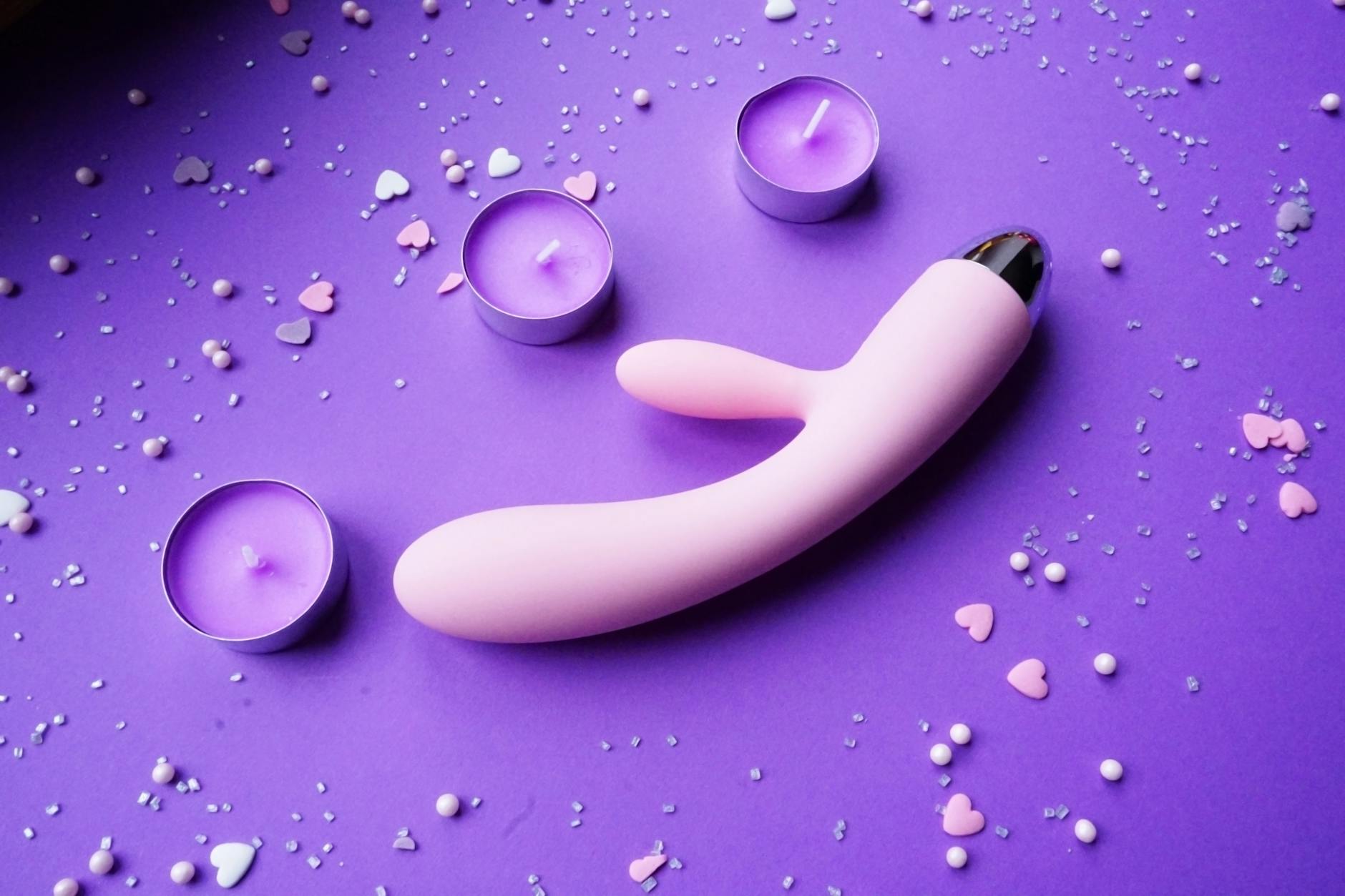 Vibrador rosa en fondo púrpura con confeti de corazones y velas.